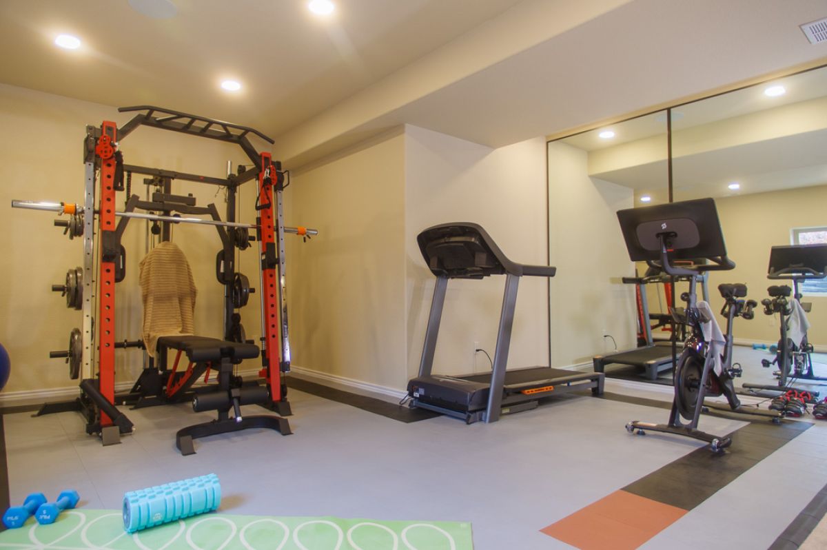 Finished basement with a home gym; weight lifting cage, treadmill, peloton bike, yoga mat, muscle rollers.