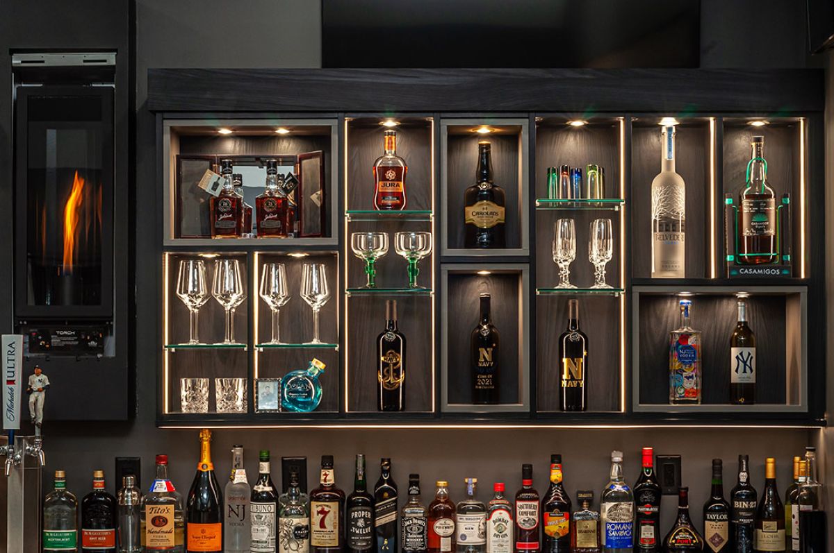 A home bar filled with glasses, bottles, and taps. Elegant presentation. Integrated lighting.