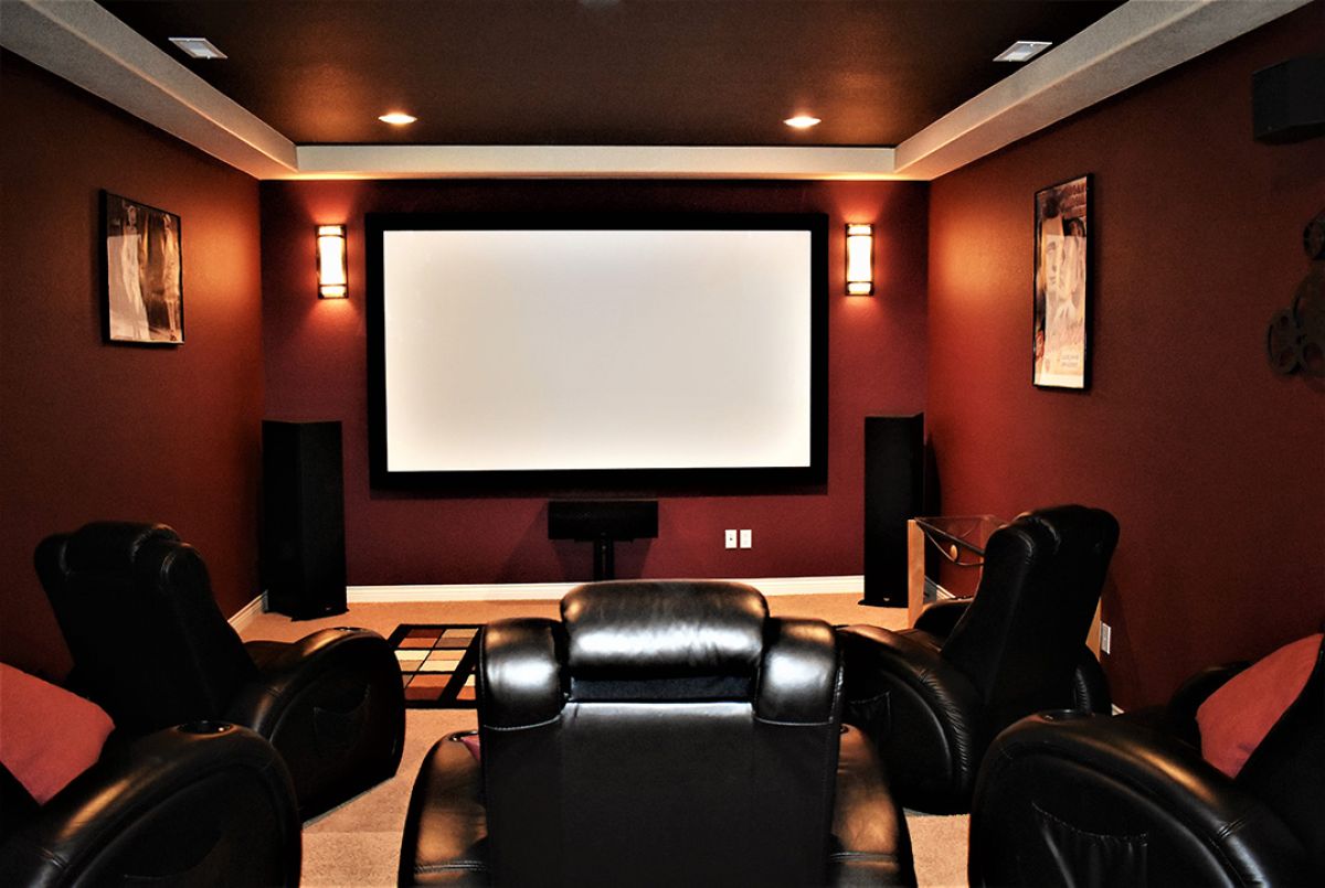A home theater with accent lighting, white screen, burgundy walls, and leather reclining chairs.